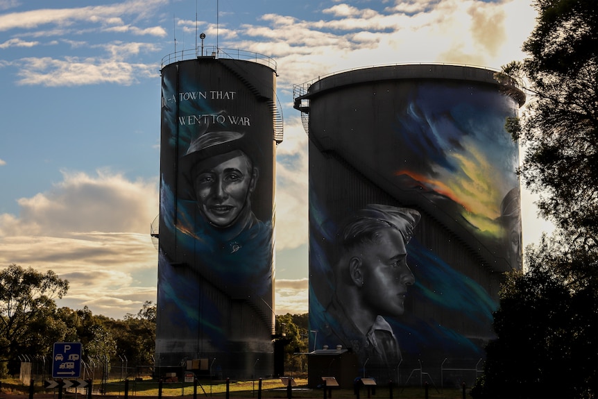 Two large concrete water towers with colourful artwork of soldiers and text beneath an afternoon skyline