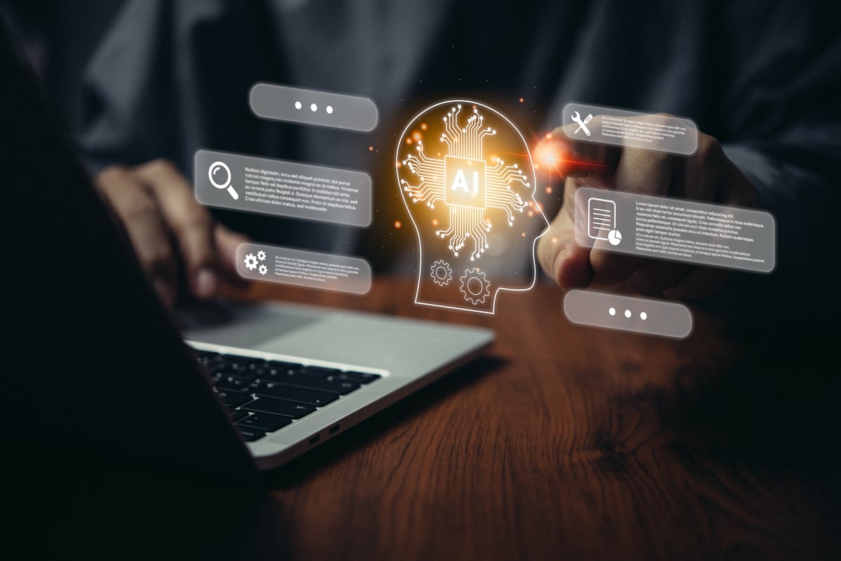 A person using a laptop and a graphic of a human head with the word AI written inside it.