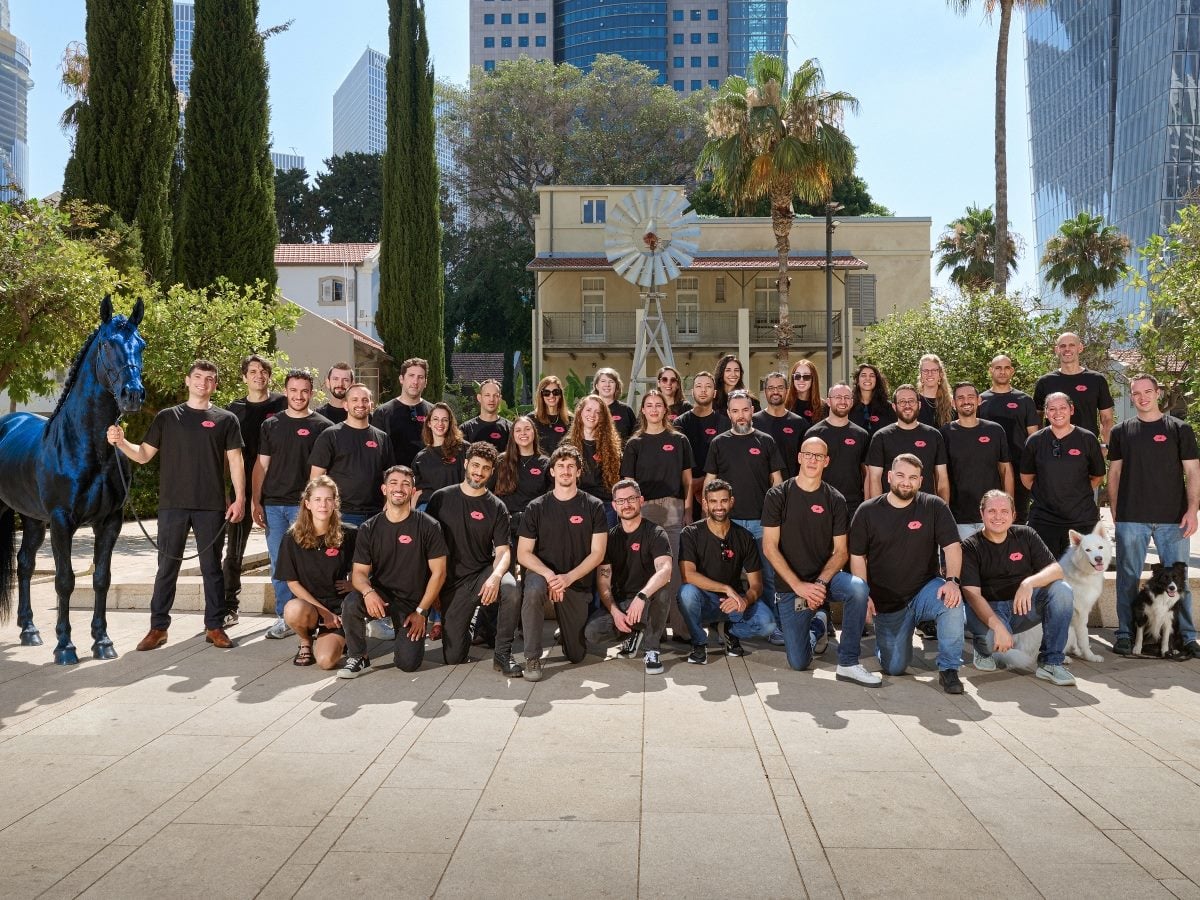Group photo of the Encore AI team gathered outdoors in a courtyard, with employees wearing matching black company T-shirts and posing in front of a restored historic building featuring a windmill. Modern office towers, palm trees and cypress trees frame the background, while a blue horse sculpture stands on the left and two dogs sit with team members on the right.
