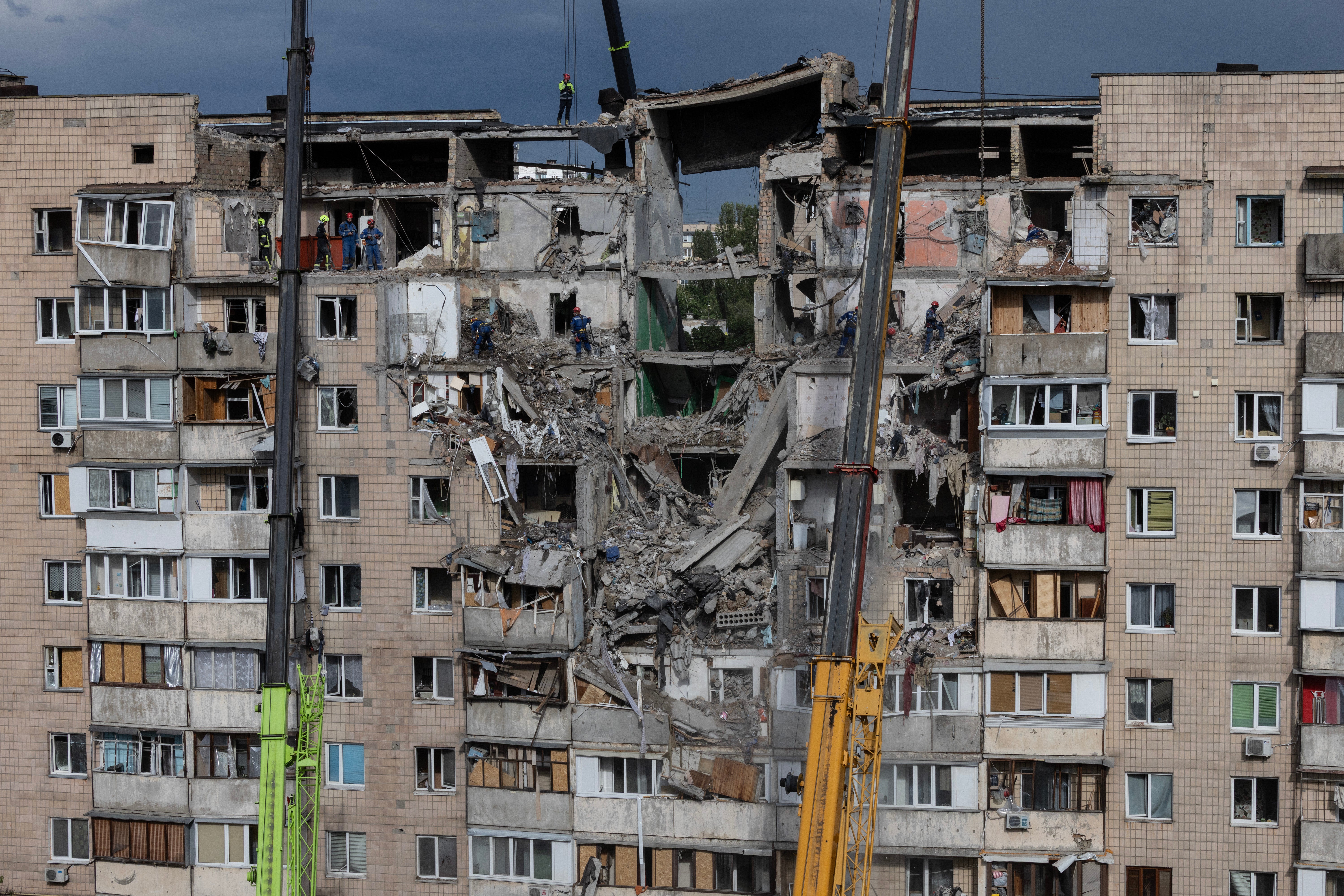 Emergency workers and machinery clear debris from the scene of an attack as Russian missiles and drones struck Kyiv overnight