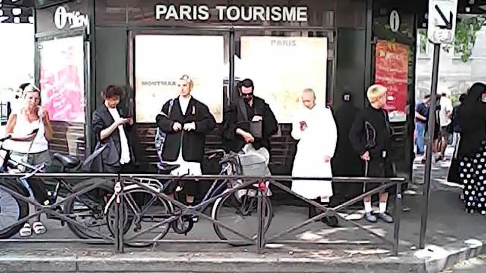 People stand in front of a wall bearing the words "Paris Tourisme"