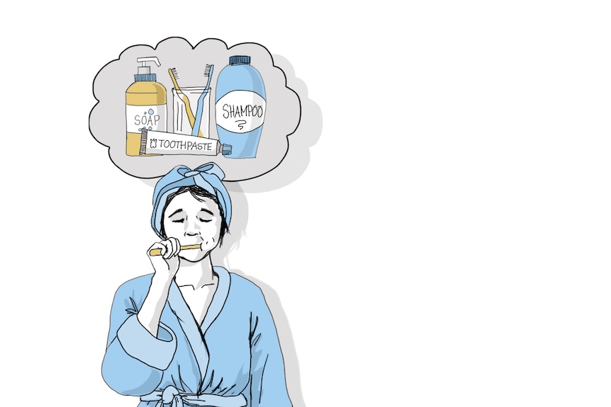 Woman in blue dressing gown brushing teeth, towel wrapped on head, cloud of soap, toothpaste and two brushes in a glass behind.
