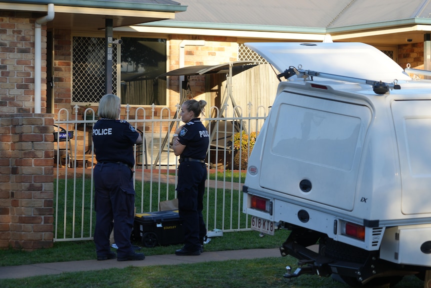 Two policewomen stand outside a home talking.