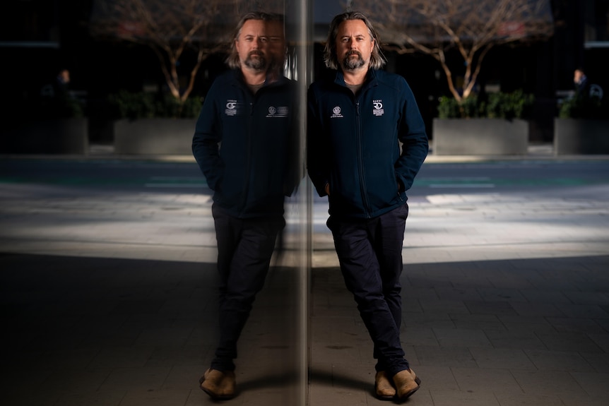 A marine scientist leans against a reflective surface.