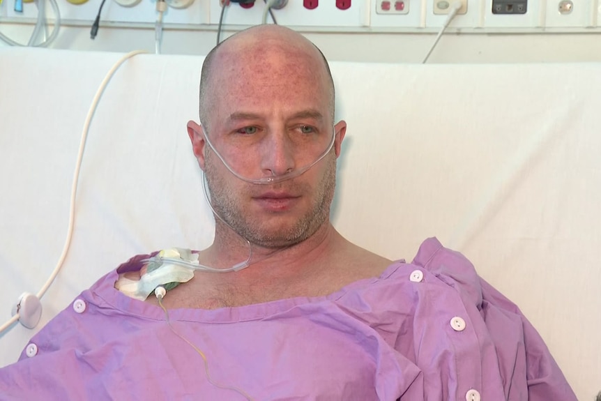 A man in a purple hospital gown with an oxygen tube.