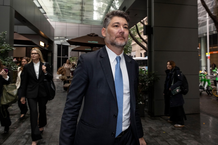 Mr Fang wearing a suit and blue tie while walking down a street path