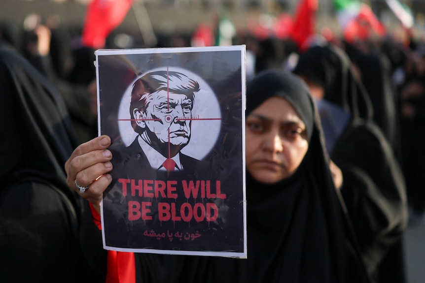 A woman in a black hijab holds up a sign of Trump with a crosshair over his face, and the words "THERE WILL BE BLOOD".