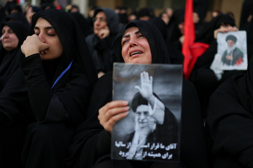 Dozens of women wearing black look devastated, some holding pictures of late Ayatollah Ali Khamenei.