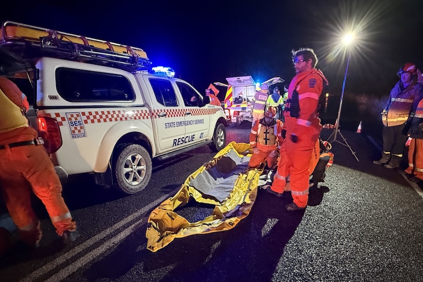 SES volunteers in orange suits gather around white emergency ahead of the rescue of a man stranded in floodwater.
