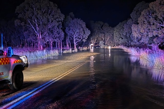 A police car with red lights flashing at a flooded road at night