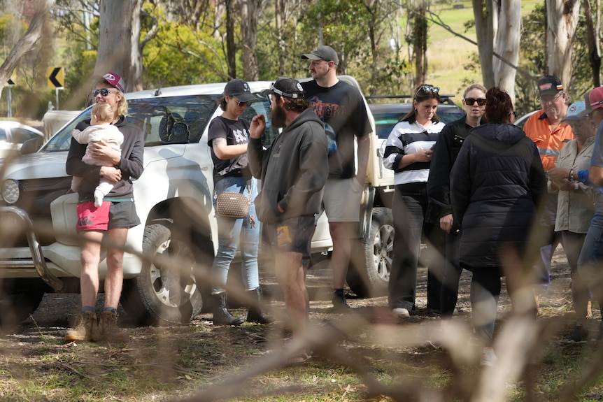 A group of people standing around cars in bushland.