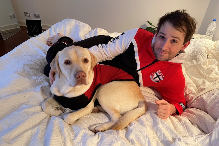 Laurence smiles while he lies on the bed with his dog