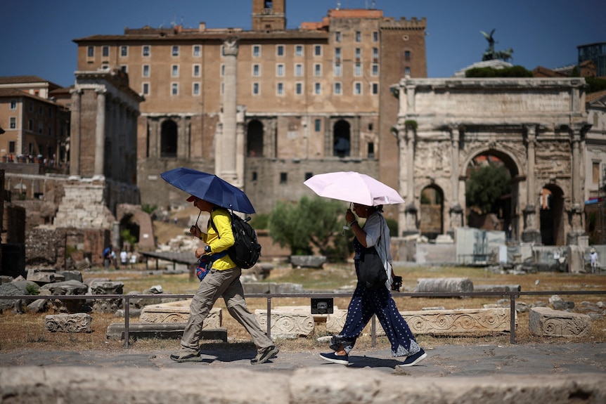 People use umbrellas to shelter from the sun near an archeological site.