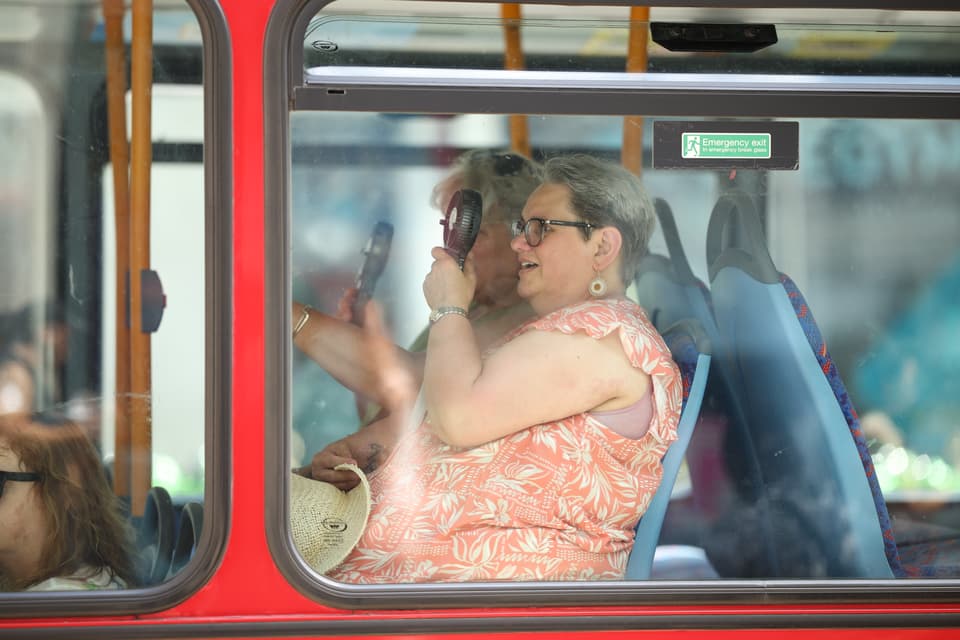 <p>A woman uses an electric fan to cool down on a bus during the heatwave</p>