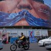 Vehicles drive past a billboard with an illustration showing the Strait of Hormuz and the sewn lips of President Trump in a square in downtown Tehran, Iran, May 2.