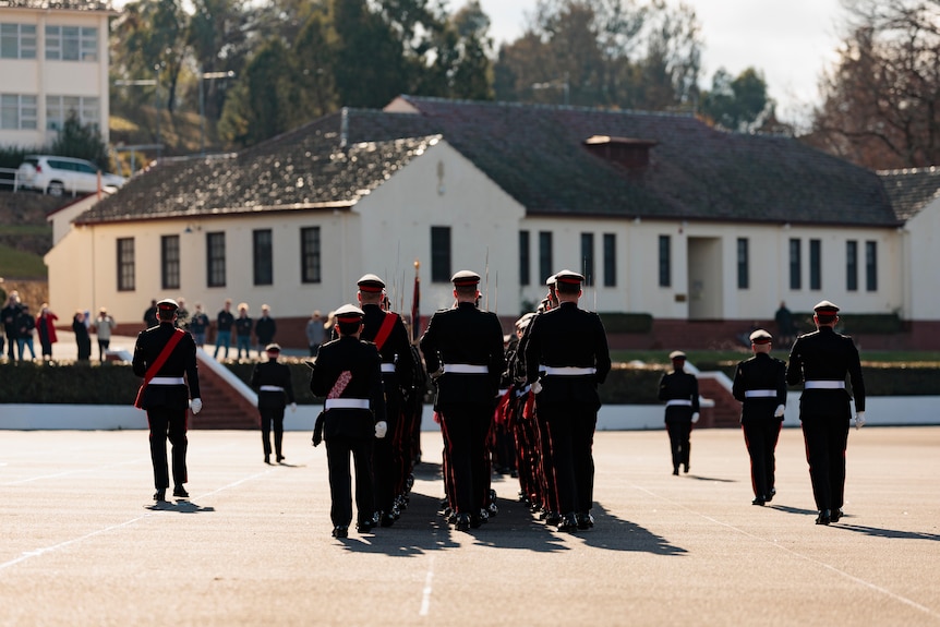 A view from behind of military graduates in full dress uniform, marching.