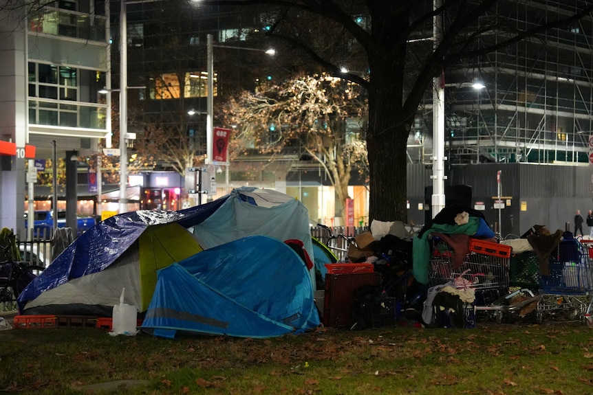 A collection of partially damaged tents erected together in a city centre next to trolleys full of blankets and clothing.