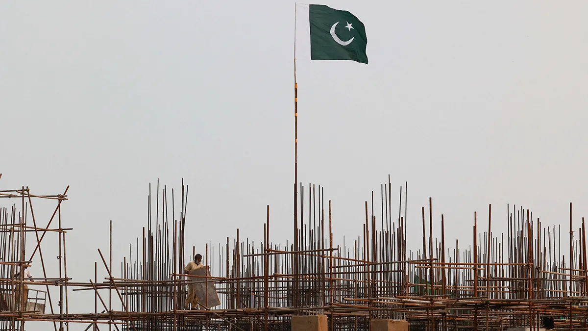 A Pakistani flag flutters above iron scaffolding as a worker operates on a construction site - REUTERS/ AKHTAR SOOMRO