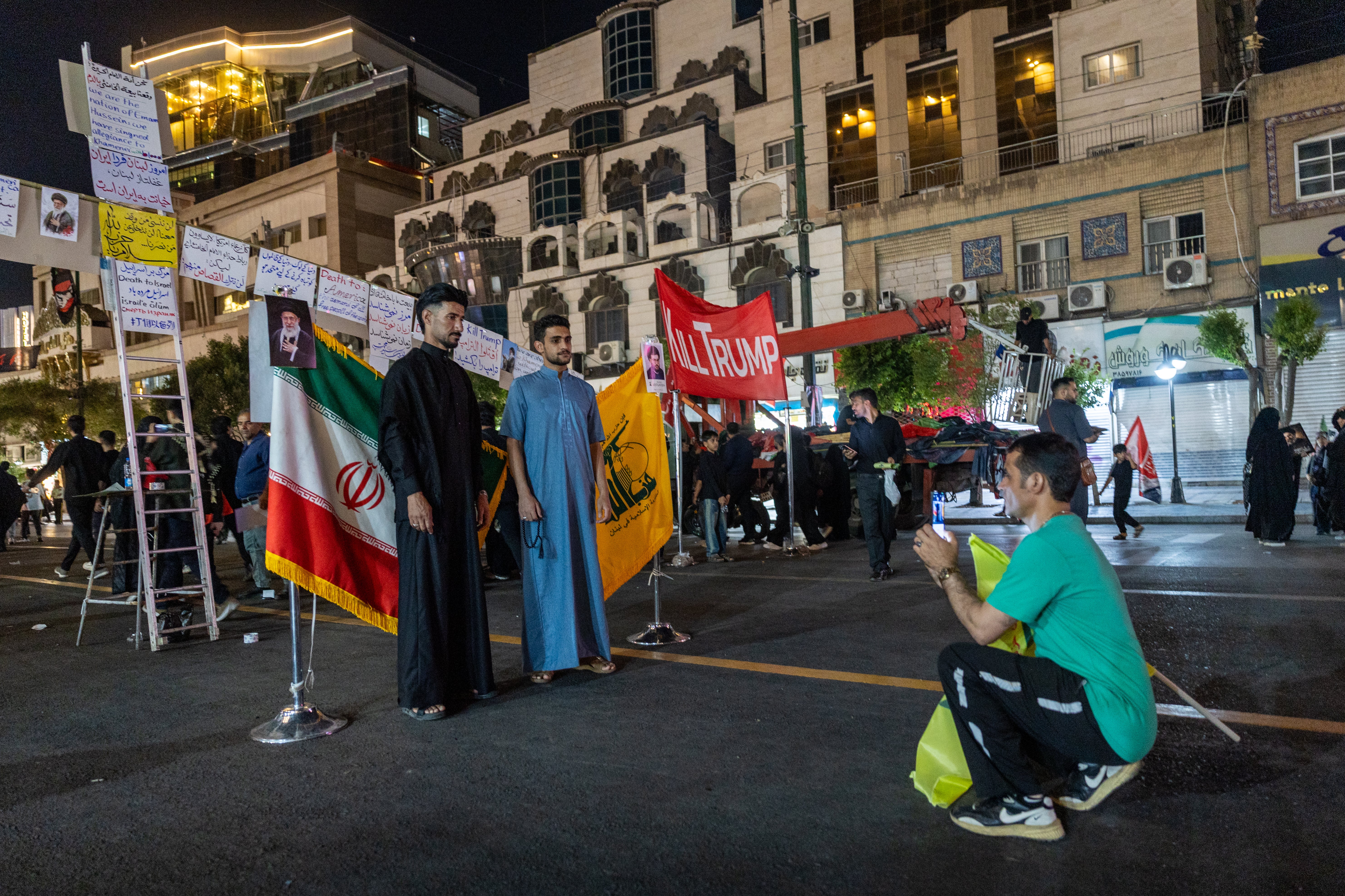 Mourners pose for keepsake photos in front of the Iranian flag and the flag of Hezbollah in Lebanon near the Imam Reza Shrine