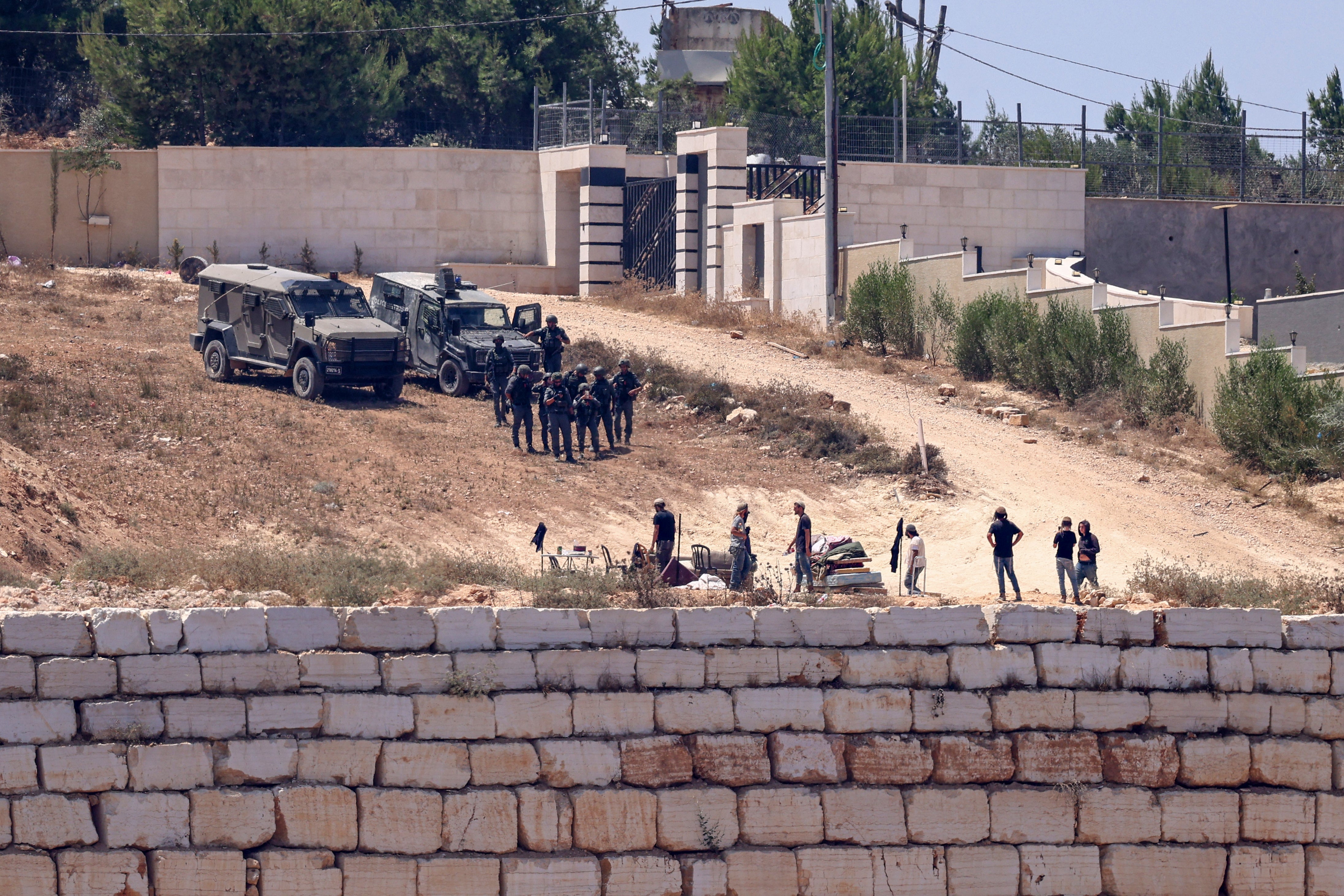 Israeli soldiers (top) stand guard next to settlers in front of the Palestinian houses in the village of Qusra, south of Nablus, in the occupied West Bank