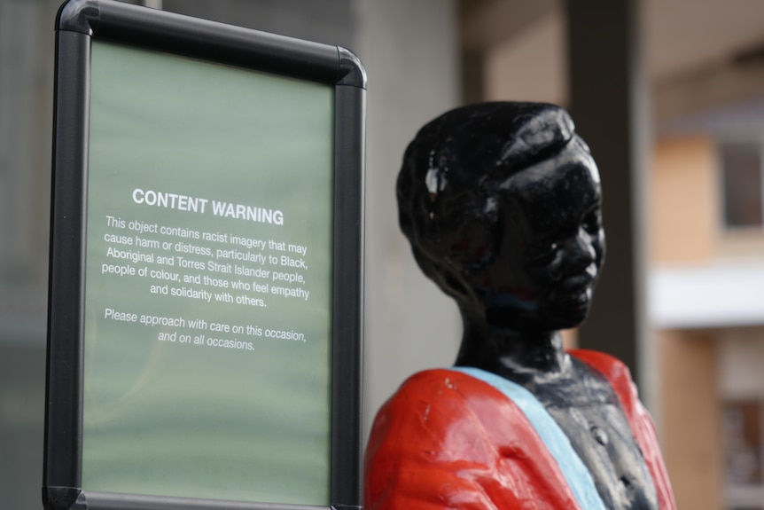 A content warning sign placed next to a miniature statue of an African American boy.