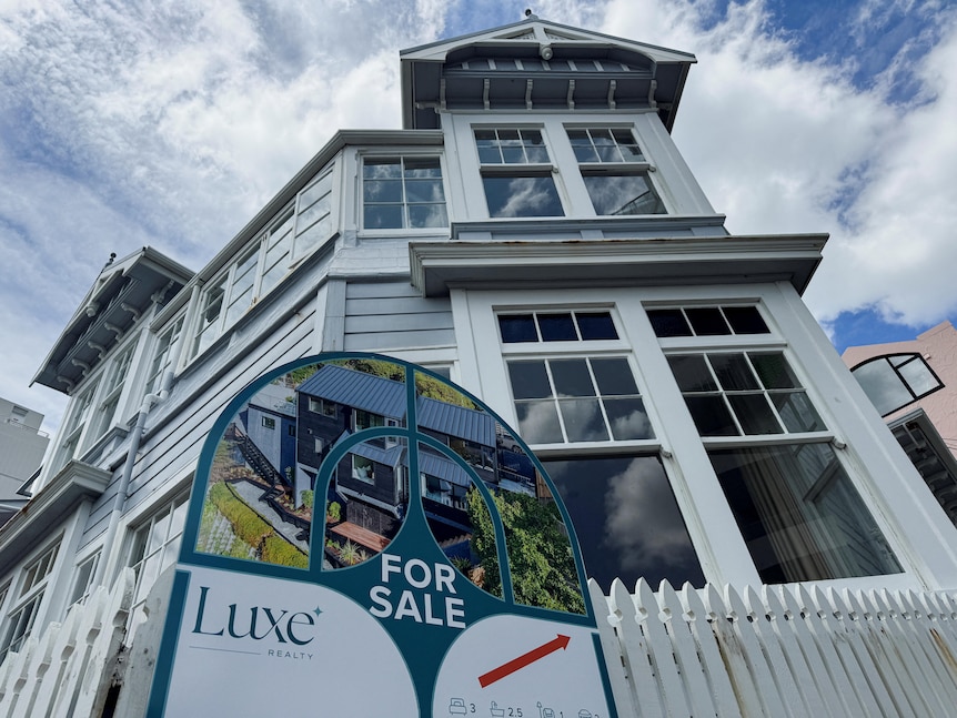 A for sale sign sits outside a two-storey property with a white picket fence