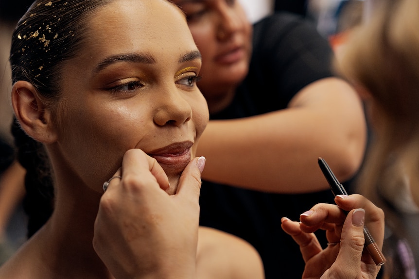 A model having make-up applied to face by a make-up artist, backstage at a runway show.