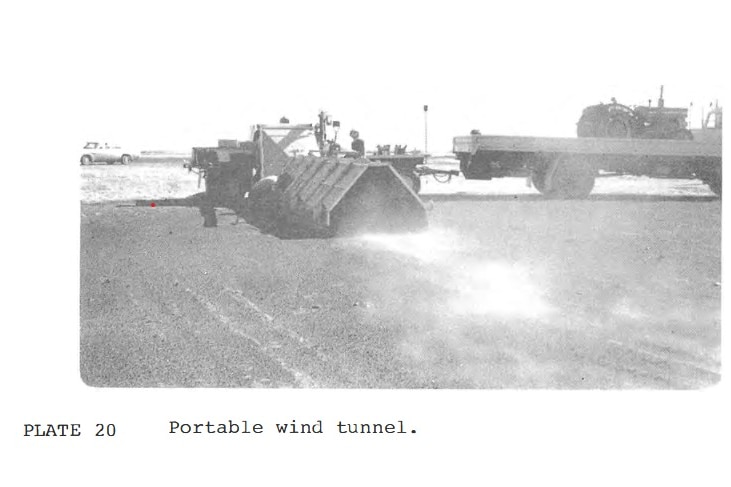 A grainy black-and-white photo of men examining a small above-ground metal tunnel.