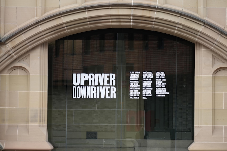 Glass doors outside an art gallery with the words "Upriver Downriver" printed on them