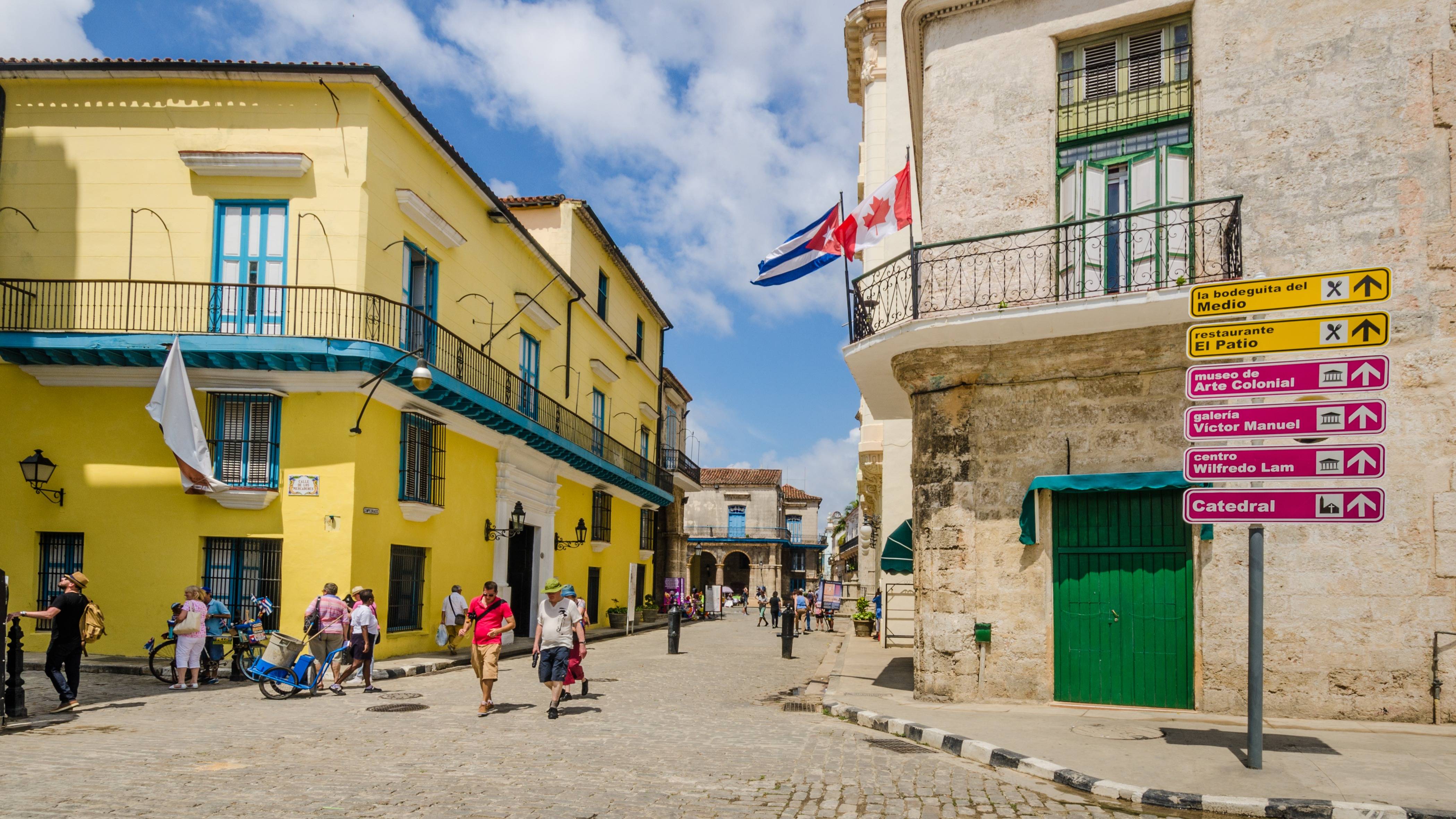 Tourists walking as Cuban and Canadian flags fly from one of the buildings on the corner of Mercaderes and Emperado in the Plaza de la Catedral district in Havana, Cuba