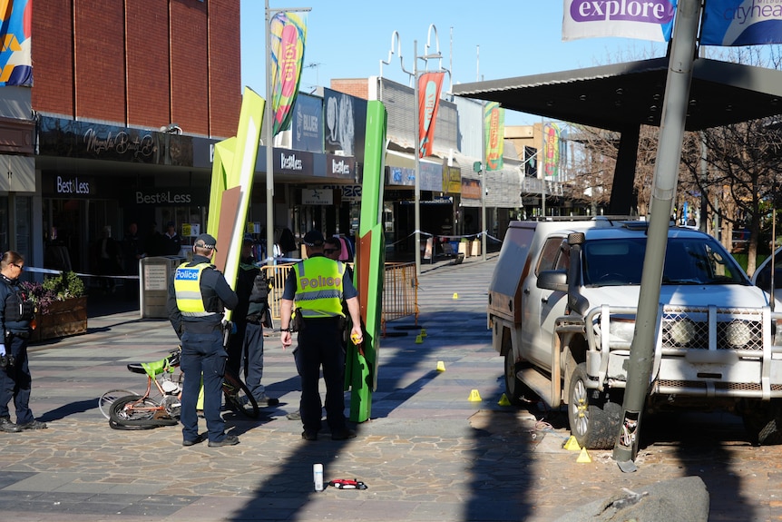 A white ford ute which has collided with a light pole in a pedestrian mall
