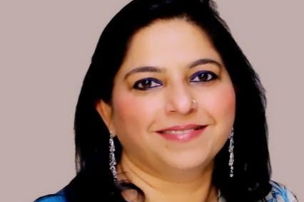 Priya smiles, has long dark hair is wearing a blue printed silk kurta.
