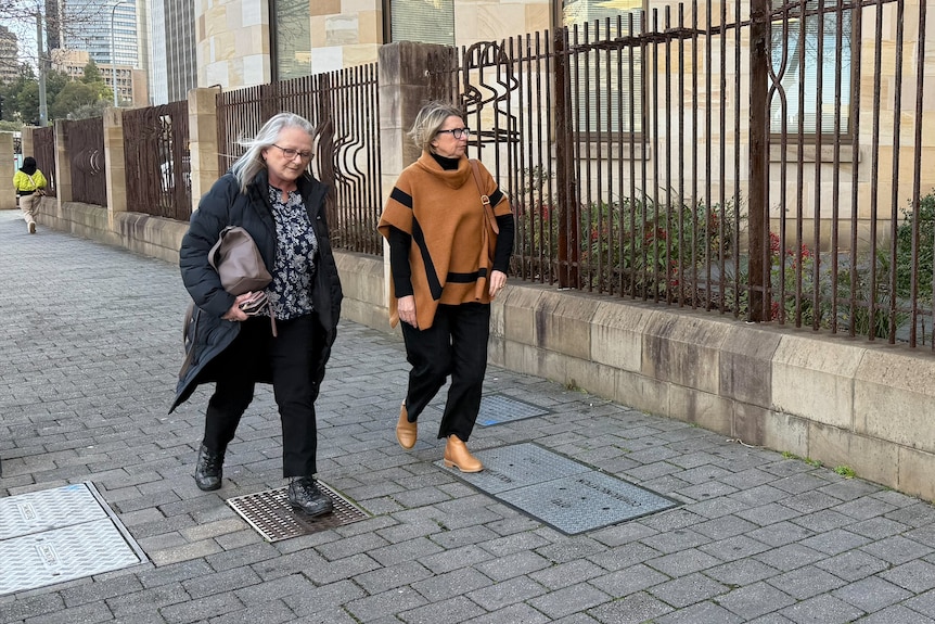 Two women walk along a paved grey footpath