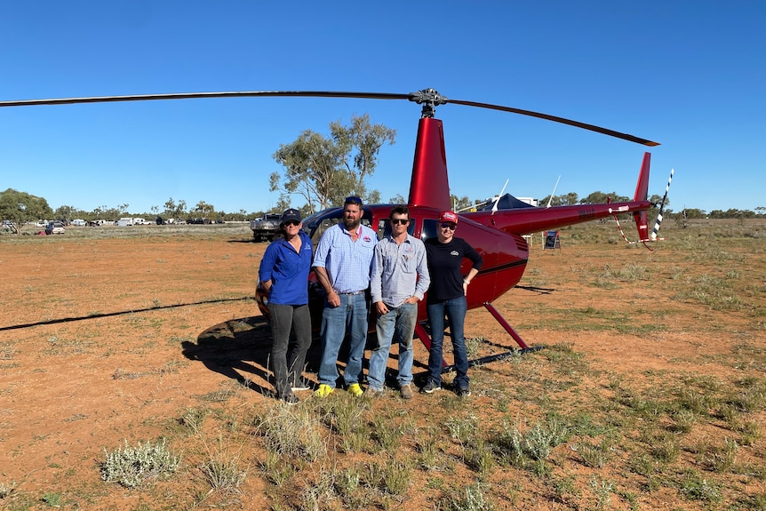 four people stand in front of red helicopter