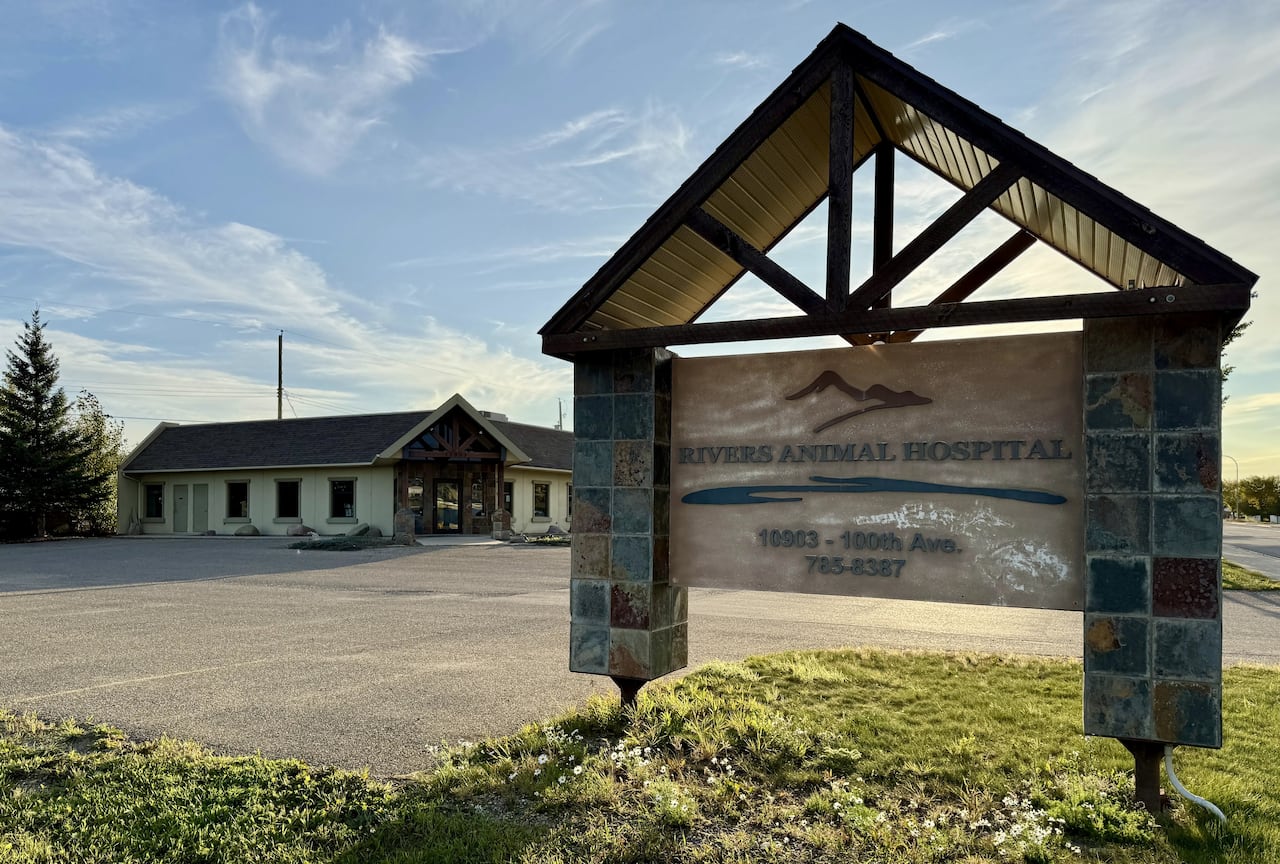A sign that says "Rivers Animal Hospital" in front of a parking lot and a yellow building with a brown entrance.