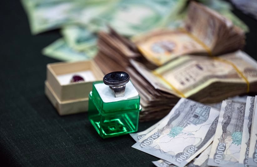 An Aqeeq (agate) ring is pictured next to Iraqi dinar and US dollar banknotes are laid out on a table as members of the Shia Muslim community arrive at a centre in Iraq's southern city of Basra accepting charity donations to aid people affected by the ongoing war in Iran and Lebanon.