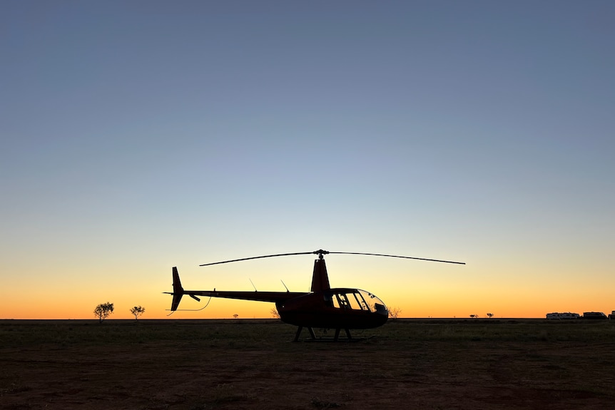the silhouette of a grounded helicopter against a sunset