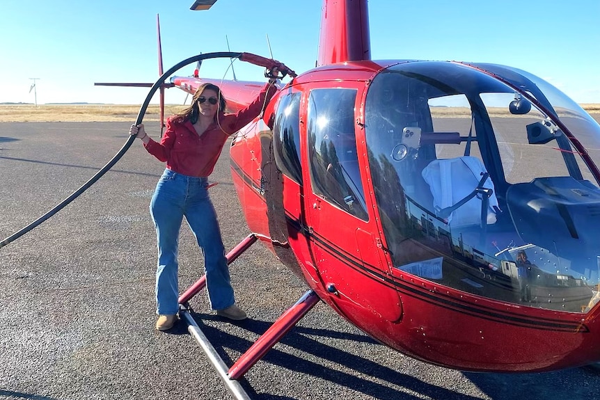 a woman holds a refuelling hose connected to a red helicopter