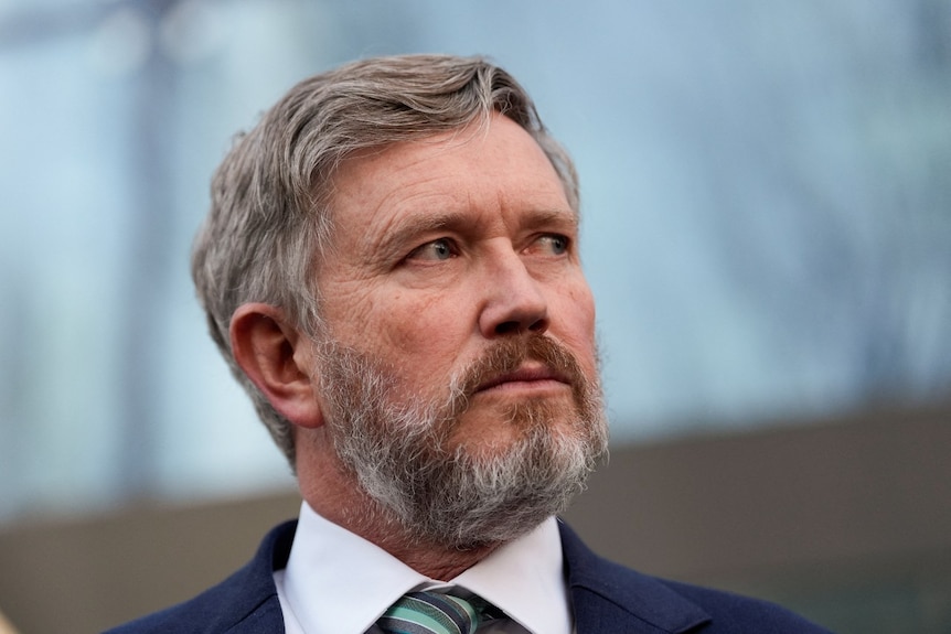 A man in a suit looks on. His face is seen from lose up.